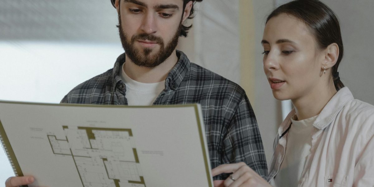 A young couple reviewing architectural plans and documents with an advisor, symbolizing the guided journey for first-time home buyers.